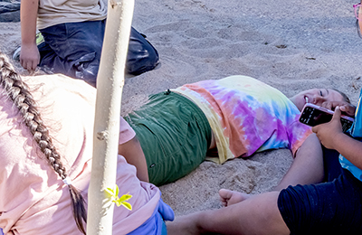 An education specialist is buried in sand by children at Spadefoot Splash